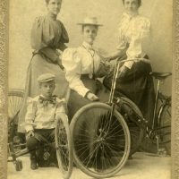 Portrait of three women and a young boy. One woman and the young boy both are holding up bicycles.