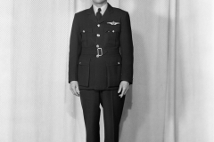Black and white wide shot portrait of a man in an RAF or RCAF uniform. He is wearing a EFTS Instructor cap badge on his hat. There is also another double wing badge on his jacket.